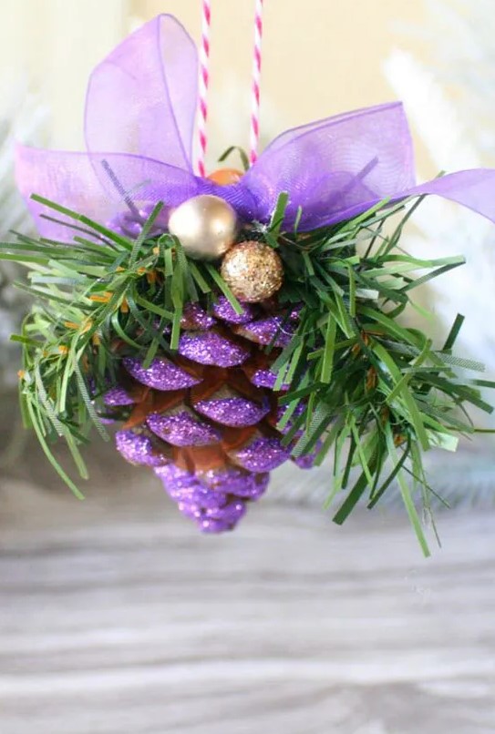 dip pinecones in purple glitter for a fun and bright look, when paired with gold balls this is a bright ornament to hang in your home