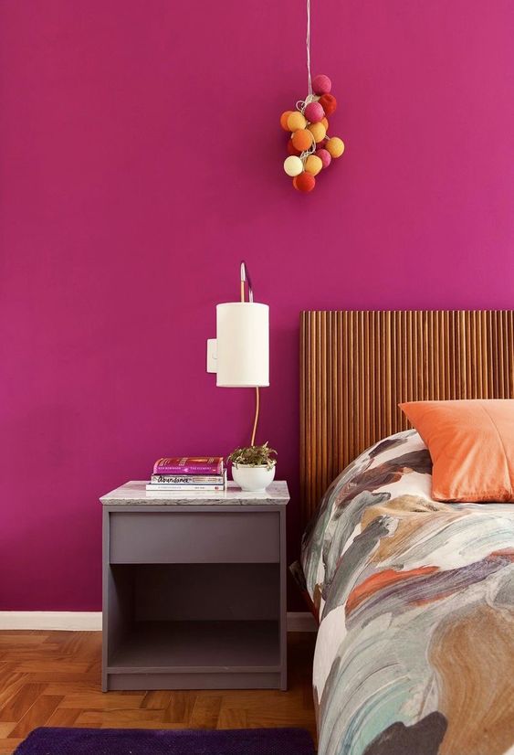 a bold magenta bedroom with a bed with a slat headboard, a lilac nightstand and a catchy pendant lamp reminding of an arrangement of balloons