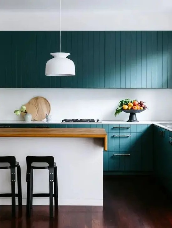 a stunning turquoise coastal kitchen with beadboard cabinets, a white kitchen island with a stained countertop, black stools and a white pendant lamp