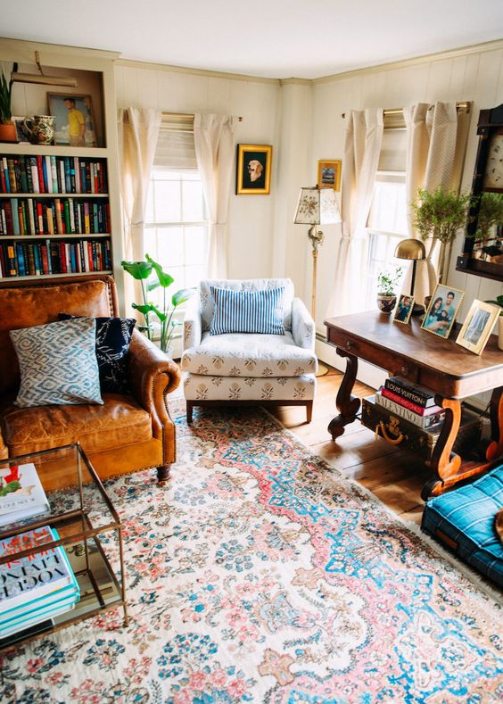 a retro living room with bookcases, a leather and a printed upholstered chair, a heavy vintage wooden table and some potted greenery