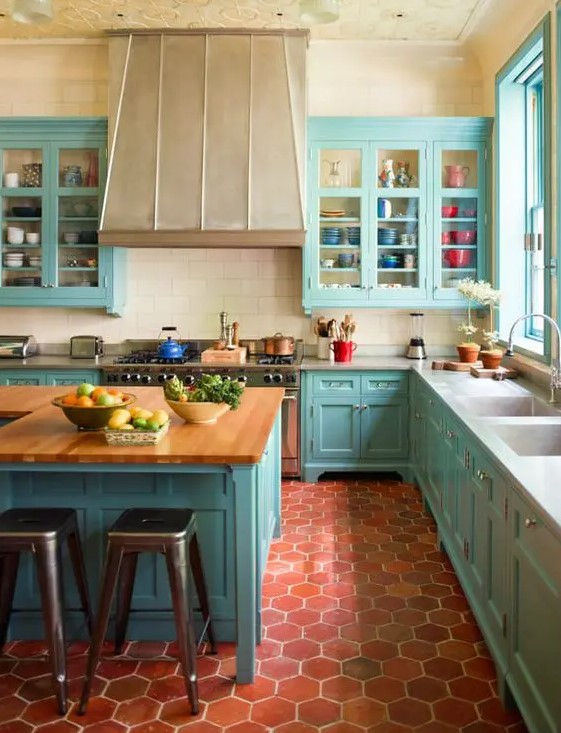 a bright blue kitchen with terracotta tile on the floor, a large vintage hood, butcher block countertops and a patterned ceiling