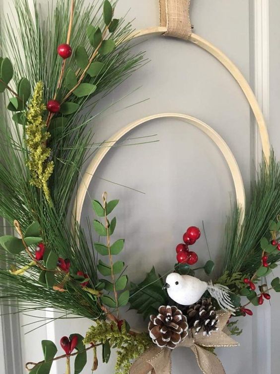a double embroidery hoop Christmas wreath of evergreens, berries, snowy pinecones, a bird and a ribbon bow is lovely