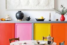 06 a colorful kitchen with bold doors, and a round table, wooden chairs and a pretty textural artwork and red touches