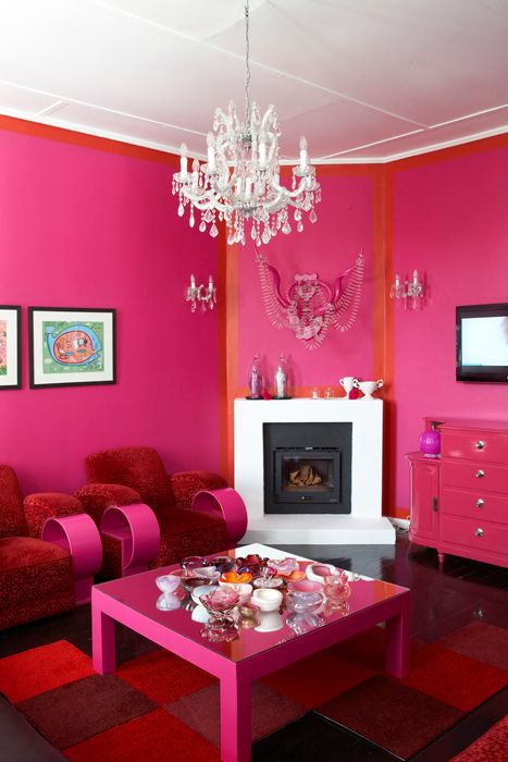 a magenta and orange living room with a built-in fireplace, red and pink furniture, a crystal chandelier and a bold rug