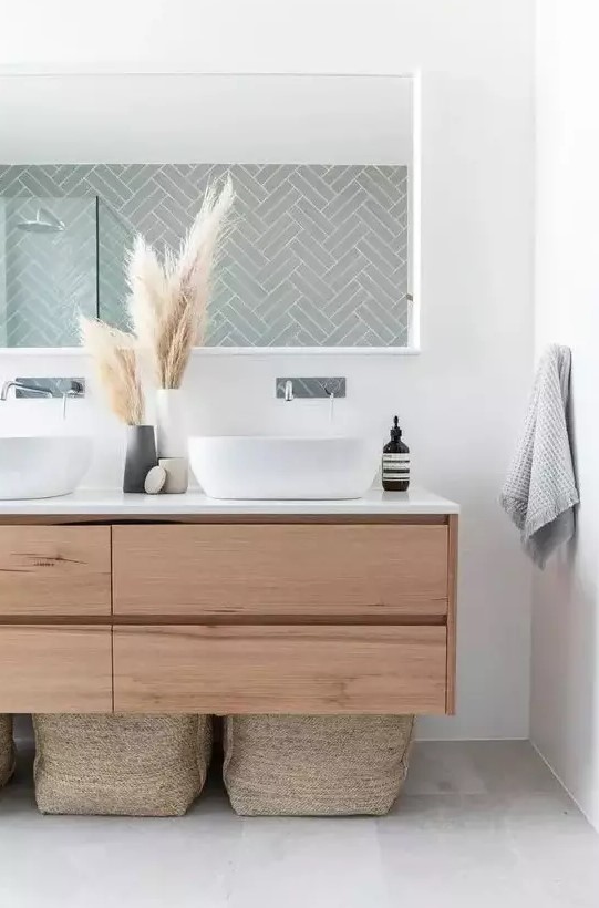 a boho bathroom with a sleek wooden floating vanity, baskets for storage, a long mirror and pampas grass in vases