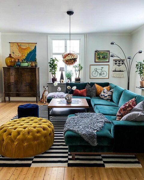 a colorful living room with an emerald sectional, mustard and navy poufs, a bold boho gallery wall and a map to personalize the space