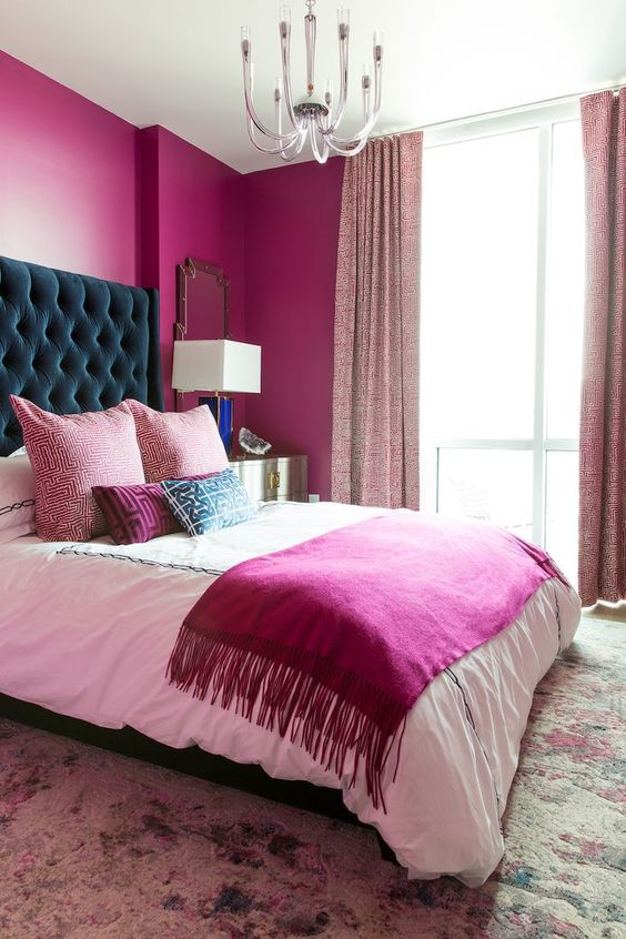 a magenta bedroom with a bed with a teal headboard, a chandelier, light pink curtains and a colorful rug is amazing