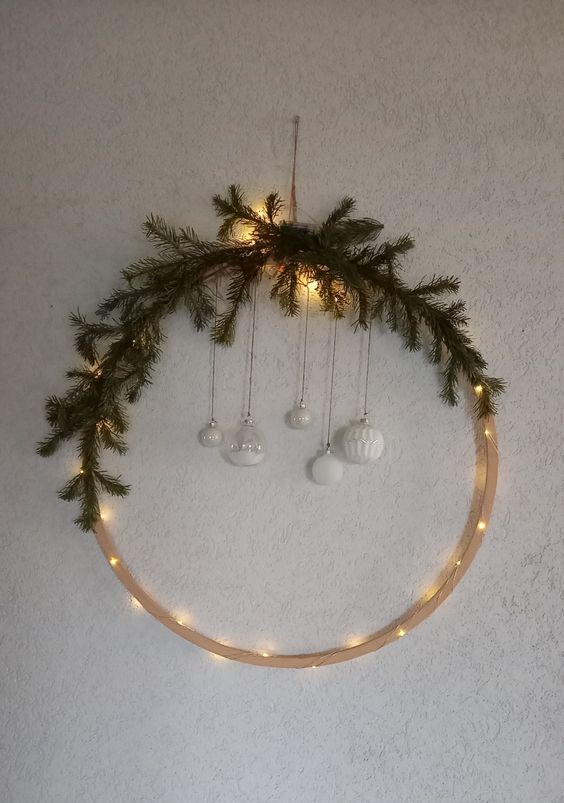 a modern Christmas wreath with lights, evergreens, white ornaments hanging down is a lovely idea for winter decor