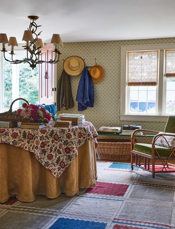 a cozy vintage-inspired interior with a bold rug, printed wallpaper, rattan furniture, floral print fabrics and books on the table