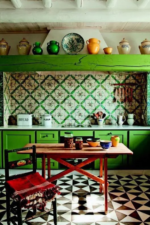 an eclectic kitchen with bold green cabinets, bright printed tiles on the backsplash, a wooden table and a chair plus colorful tableware