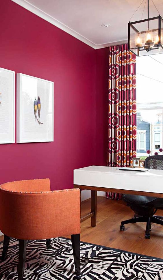 a magenta home office, a white desk, a black chair, an orange one, a printed rug and crutains for a bold look