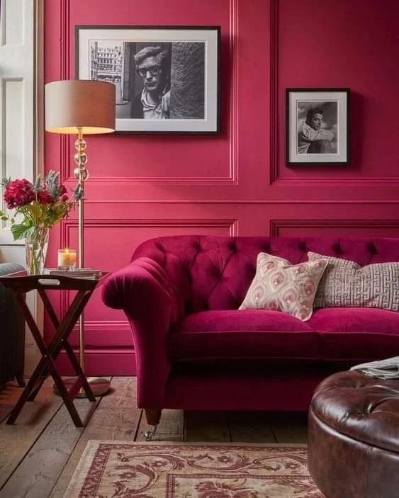 a magenta living room with a matching sofa, a leathe rottoman, some artworks and a side table plus a floor lamp