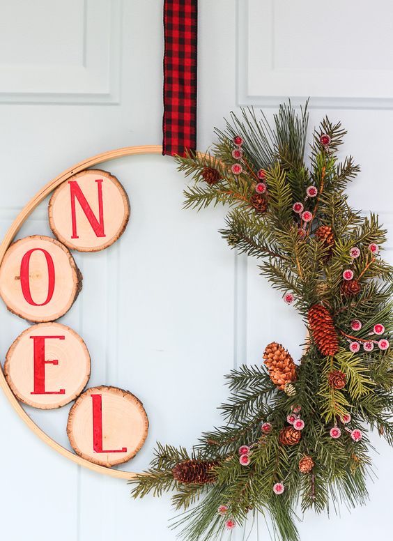 a rustic Christmas wreath with evegreens, berries and pinecones, tree slices with red letters and a plaid ribbon on top
