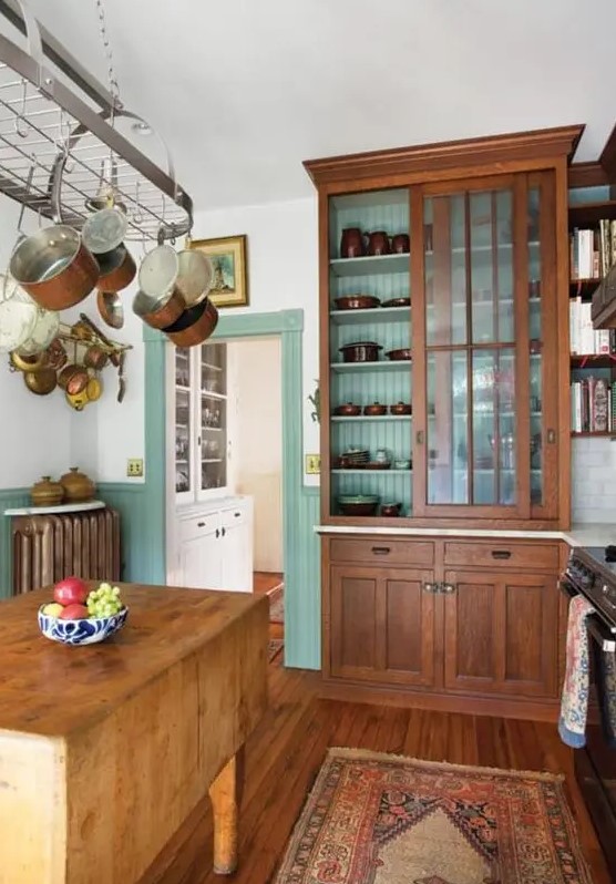 a chic vintage kitchen with mint green paneling, stained vintage furniture, a folding table as a kitchen island, a hanger with pans