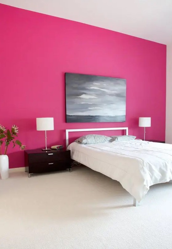 a minimalist bedroom with a magenta accent wall, a simple bed and nightstands, a table lamp and a moory artwork