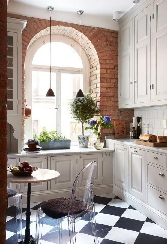 a neutral vintage kitchen with shaker style cabinets, a checked floor, potted greenery, pendant lamps and blooms, clear chairs and a round table