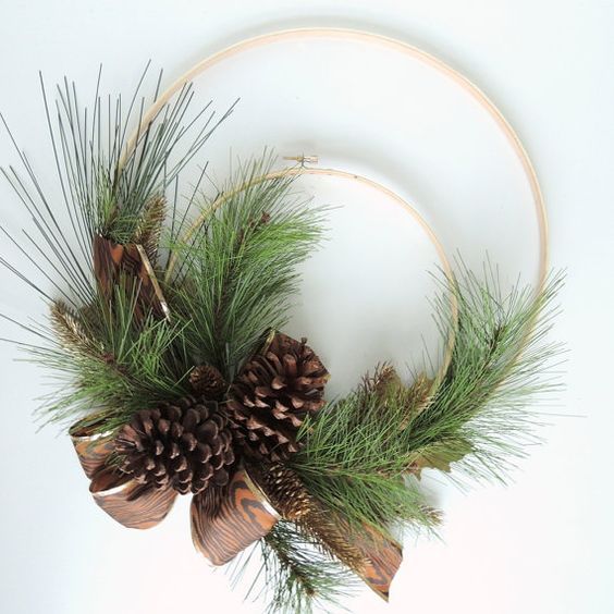 a simple rustic Christmas wreath of two embroidery hoops, evergreens, pinecones and a printed ribbon bow is cool
