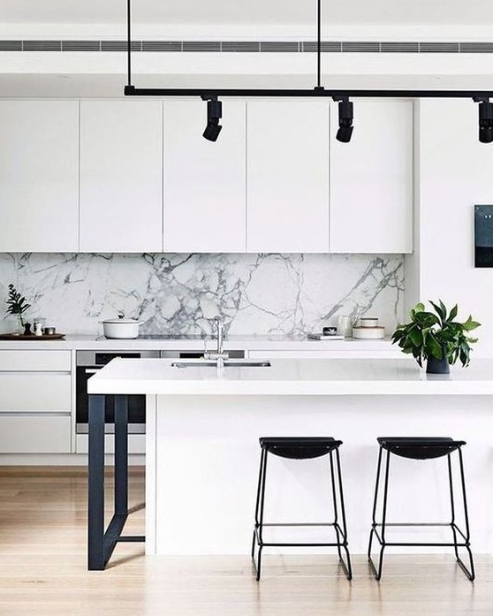 a chic white minimalist kitchen with touches of black for more drama and a white marble backsplash for a refined feel