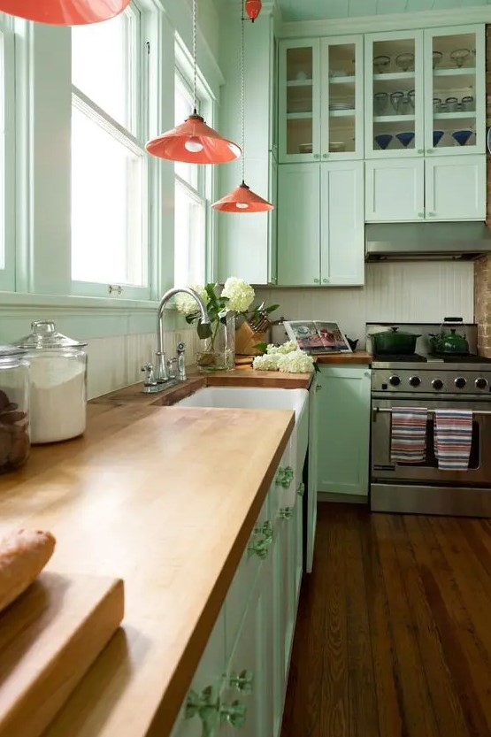 a pretty mint green kitchen with a white beadboard backsplash, butcherblock countertops, red pendant lamps and green knobs