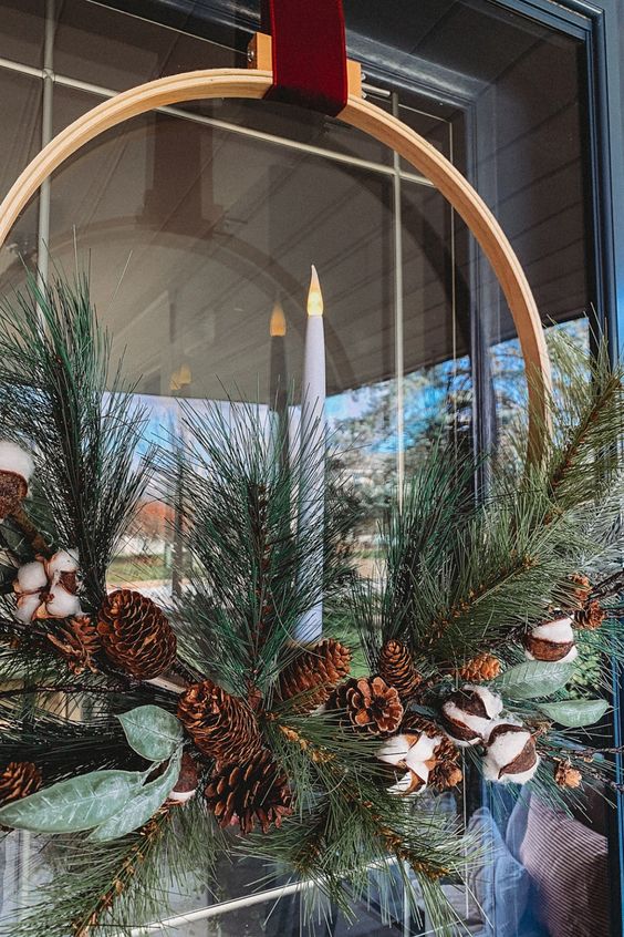 a stylish Christmas wreath of an embroidery hoop, evergreens, pinecones, cotton and leaves plus a candle in the center