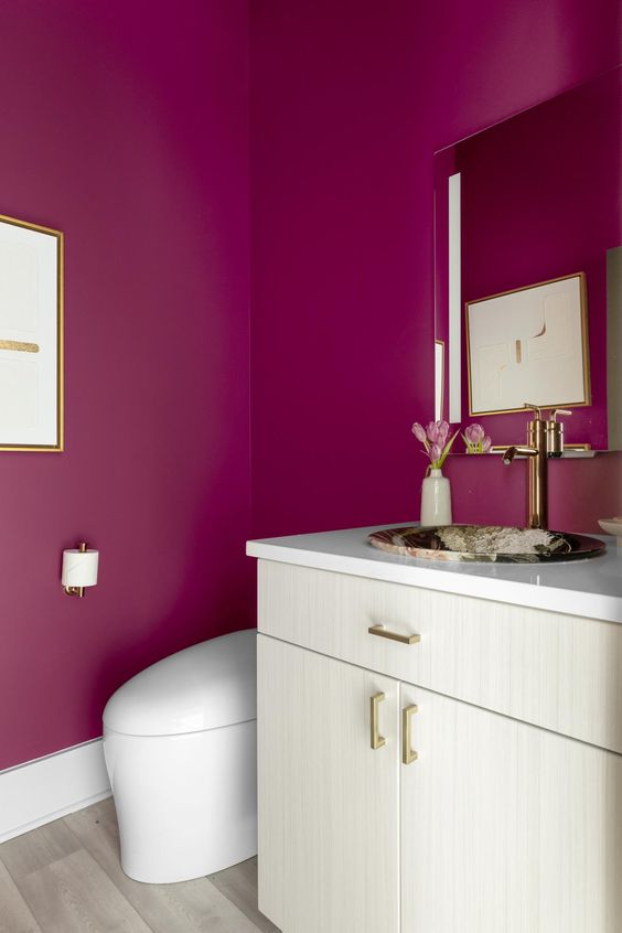 a stylish bathroom with magenta walls, a neutral vanity and a mirror with a stone sink plus a white toilet