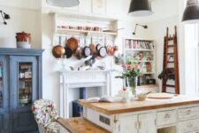 19 a vintage kitchen with white shabby chic cabinets, butcherblock countertops, black pendant lamps, a blue buffet and a vintage hearth