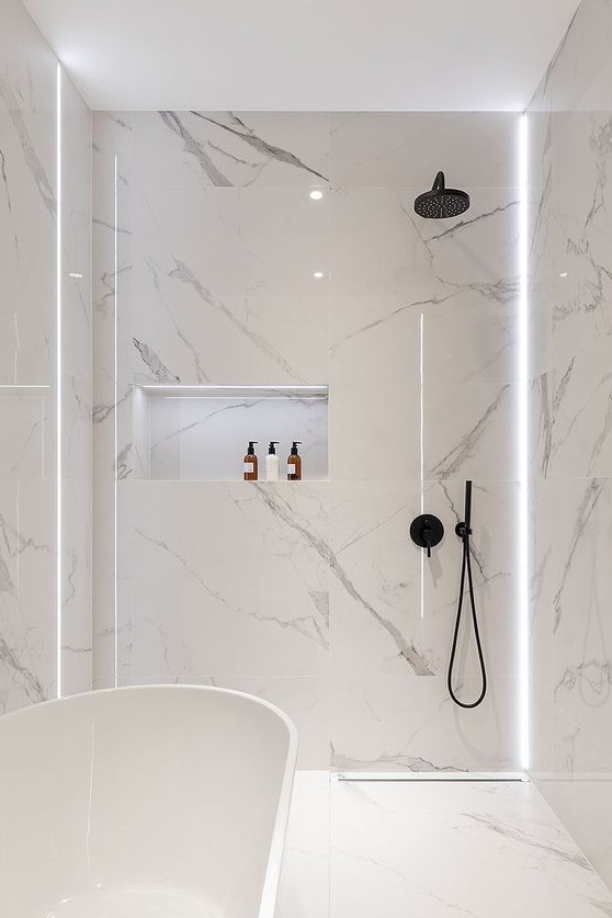 a minimalist white bathroom fully clad with marble, with a tub and a shower plus built-in lights for a refined feel