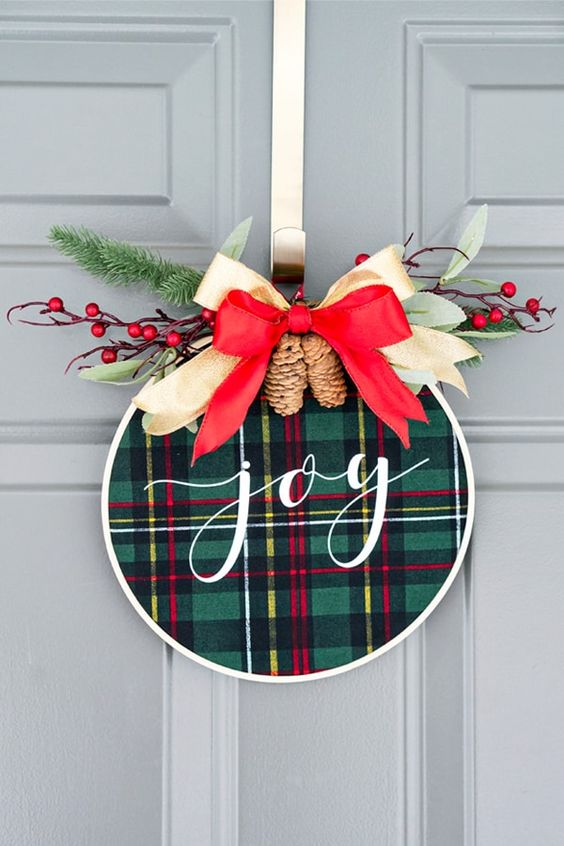 a super cool and easy to make Christmas wreath with green plaid, a red and neutral ribbon bow on top, evergreens and berries
