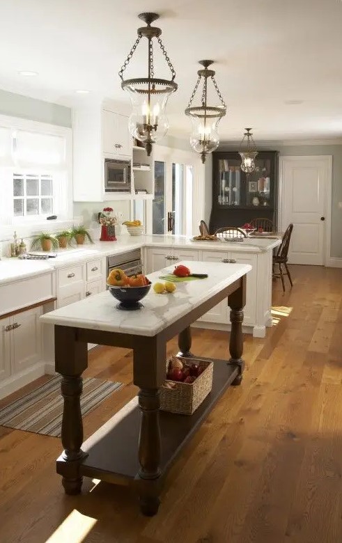 an elegant vintage kitchen with shaker style cabinets, a dark stained kitchen island, vintage chandeliers and potted herbs