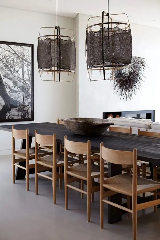 a bold and catchy dining space with a dark-stained dining table, light-stained chairs, dark pendant lamps and a bold artwork