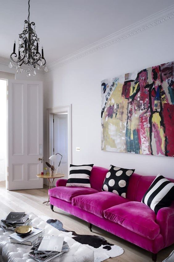 a catchy living room with a magenta sofa and printed pillows, a bold artwork, a cowhide rug and a glass coffee table plus a crystal chandelier