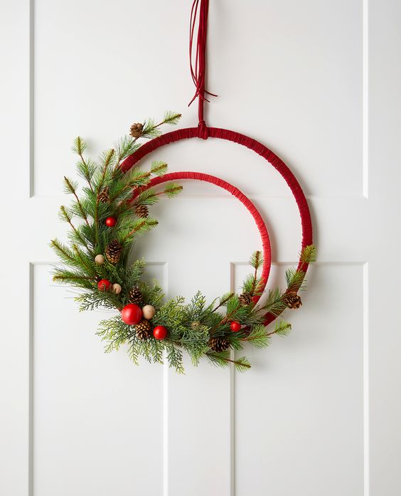 an embroidery hoop Christmas wreath in red, with evergreens, pinecones, red ornaments and wooden beads is a cool and chic idea for the holidays