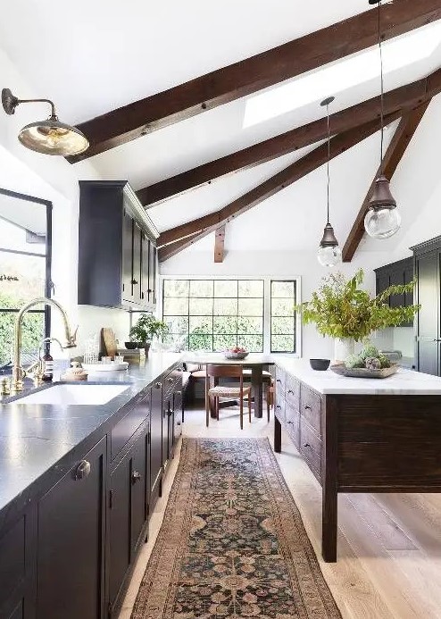 a chic modern farmhouse kitchen with a light-stained floor, dark wooden beams and a kitchen island that dominate over the space