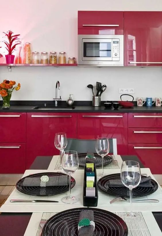 a fantastic magenta kitchen with black countertops, a matching open shelf, a black and white tablescape