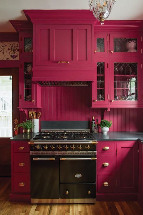 a gorgeous magenta kitchen with shaker style cabinets, dark countertops, brass touches and a black vintage-inspired cooker