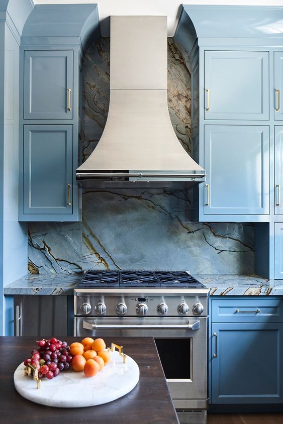 a gorgeous vintage blue kitchen with shaker style cabinets, a marble slab backsplash and gold fixtures is a lovely space