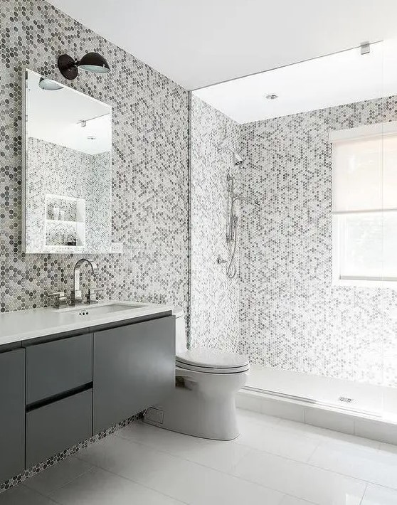 a gray kids' bathroom features grey hex tiles on the wall and they continue to the shower