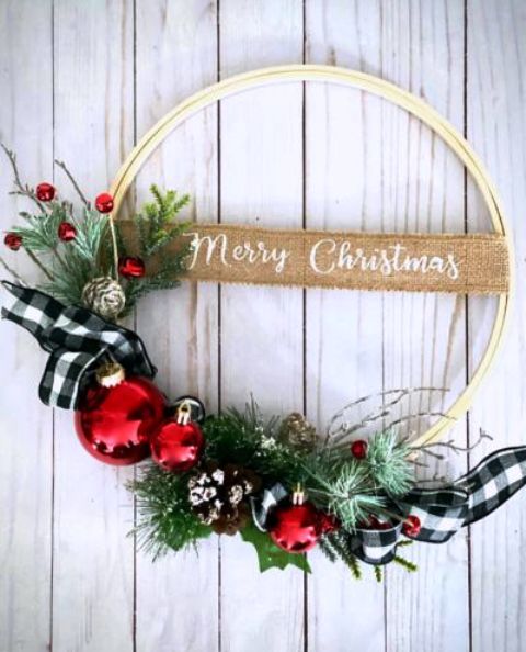 an embroidery hoop with faux evergreens, red ornaments and bells, buffalo check ribbons and snowy pinecones