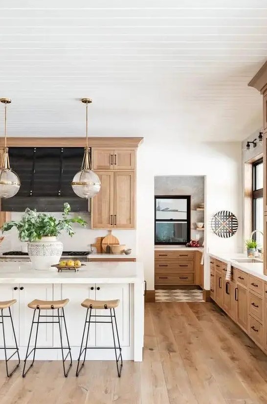 a chic modern country kitchen with light stained cabinets and hardwood floors, a white kitchen island, tall stools and pendant lamps