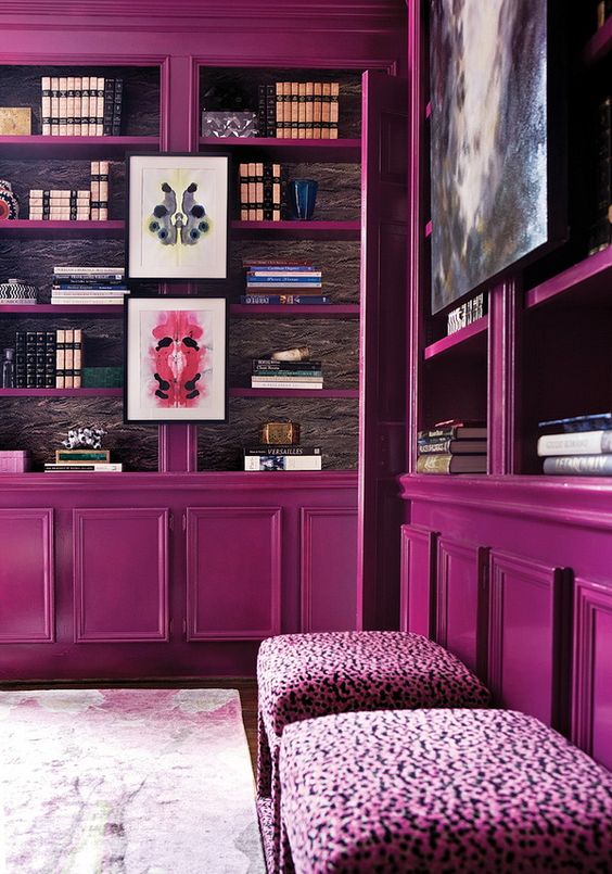 a home library done with magenta bookcases, pink stools and a printed rug just strikes with its bold color scheme