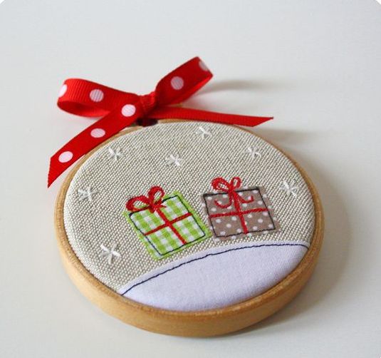 a bright Christmas ornament of an embroidery hoop and some gift applique, with a red bow on top is a cool decoration to DIY