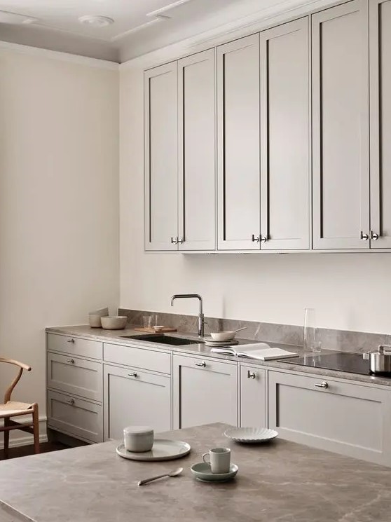 a beautiful Scandinavian greige kitchen with shaker cabinets, a brown stone countertop and a small backsplash plus a table with a matching tabletop