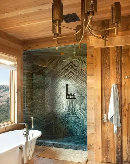 a gorgeous chalet bathroom done with light-stained wood and green marble in the shower, a tub with a view