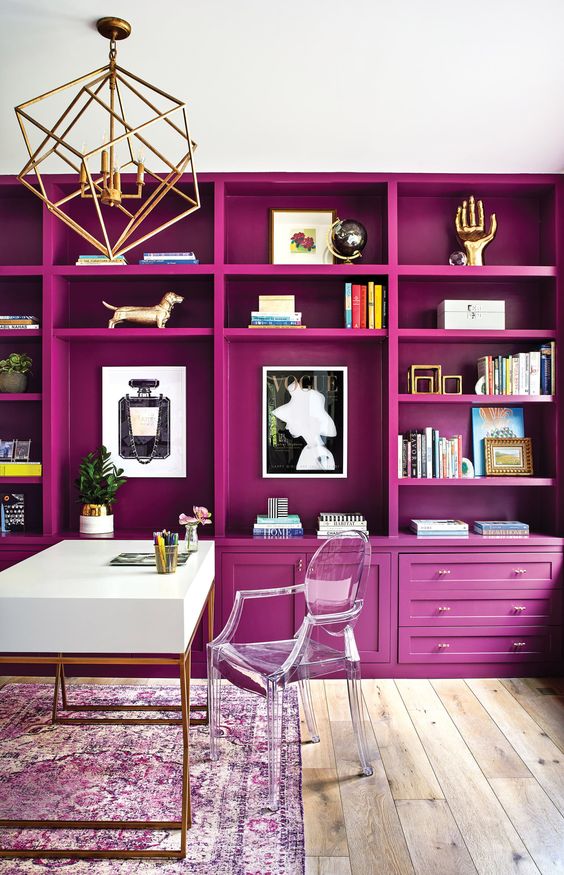 a jaw dropping home office with a magenta storage unit that creates an ambience, a white desk and a clear chair, a gold chandelier