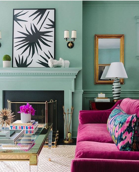 a light green living room with a fireplace and a cover, a magenta sofa with a bold pillow, a glass coffee table and chic artwork