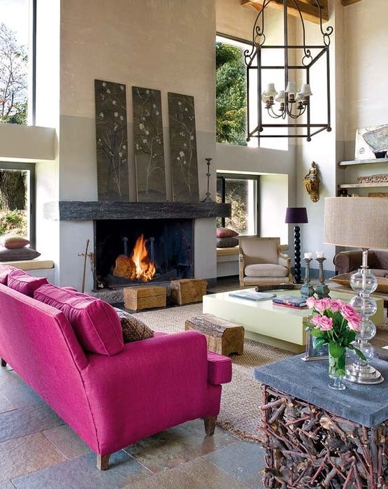 a modern living room with a fireplace, a magenta sofa, floral artworks, a creative table with wood, tree stumps and catchy lamps
