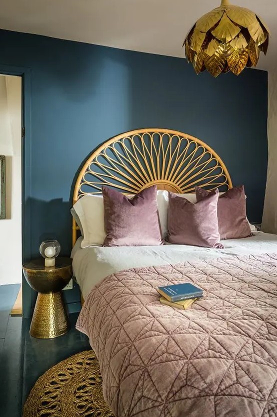a bold bedroom with a navy accent wall, a bed with a gilded headboard, a gilded nightstand, a gold petal pendant lamp