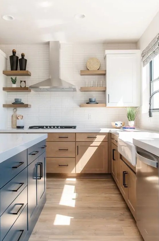 a modern farmhouse kitchen with light-stained cabinets, a navy kitchen island, white stone countertops and a skinny tile backsplash, black handles
