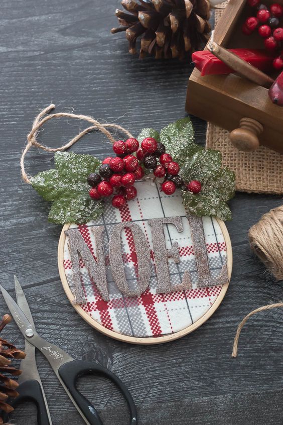 a pretty embroidery hoop Christmas ornament with red and white plaid fabric, glitter letters, snowy leaves and berries for rustic Christmas decor