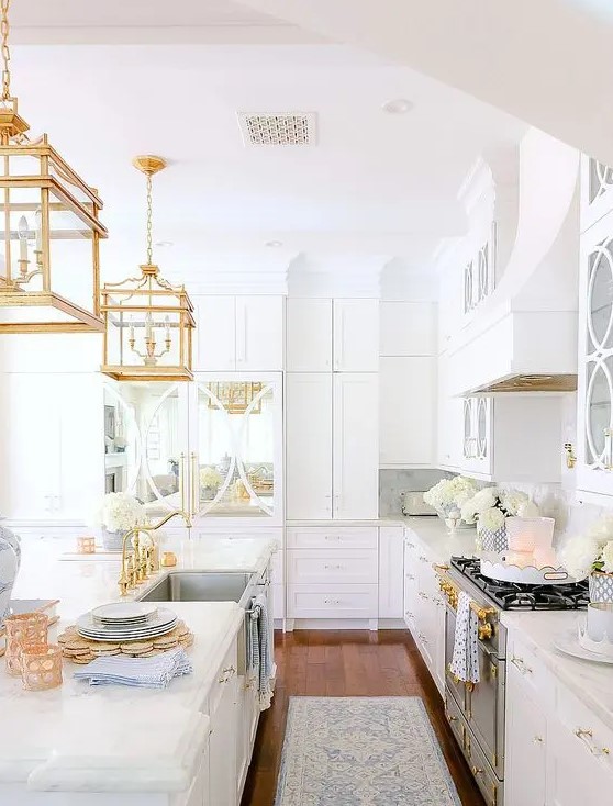 a chic and glam white kitchen with gold fixtures, refined gold pendant lamps and gold handles is a very beautiful and refined idea